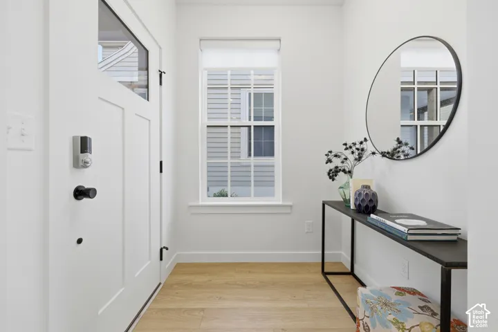 Bright entry foyer featuring a modern white panel door with glass inlay, wood-finish flooring, a white-framed window, and crisp white trim
