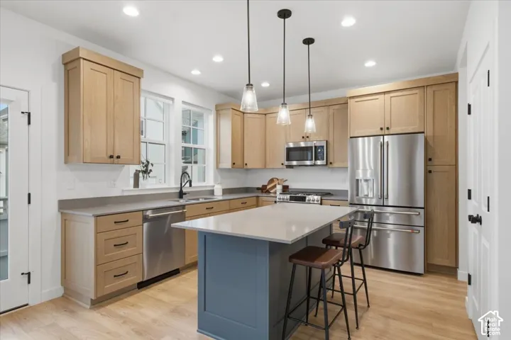 Kitchen featuring light wood-finish cabinetry, solid surface countertops, a contrasting central island, stainless steel appliances, and three glass pendant light fixtures