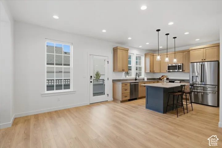 Kitchen featuring wood-finish flooring, a central island with a contrasting base, wood-tone cabinetry, stainless steel appliances, and recessed lighting