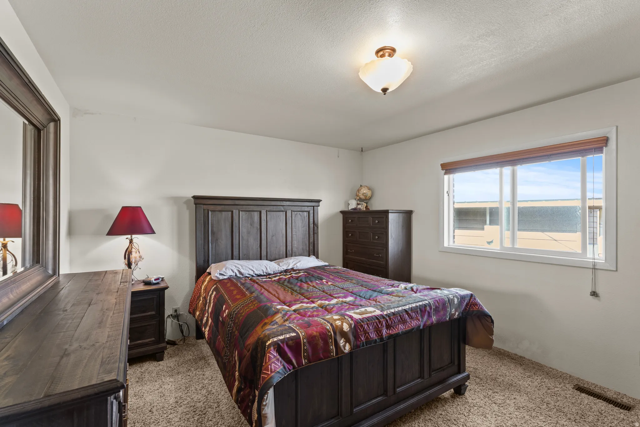 Carpeted bedroom with a single window featuring blinds, a built-in ceiling light fixture, and light-colored walls