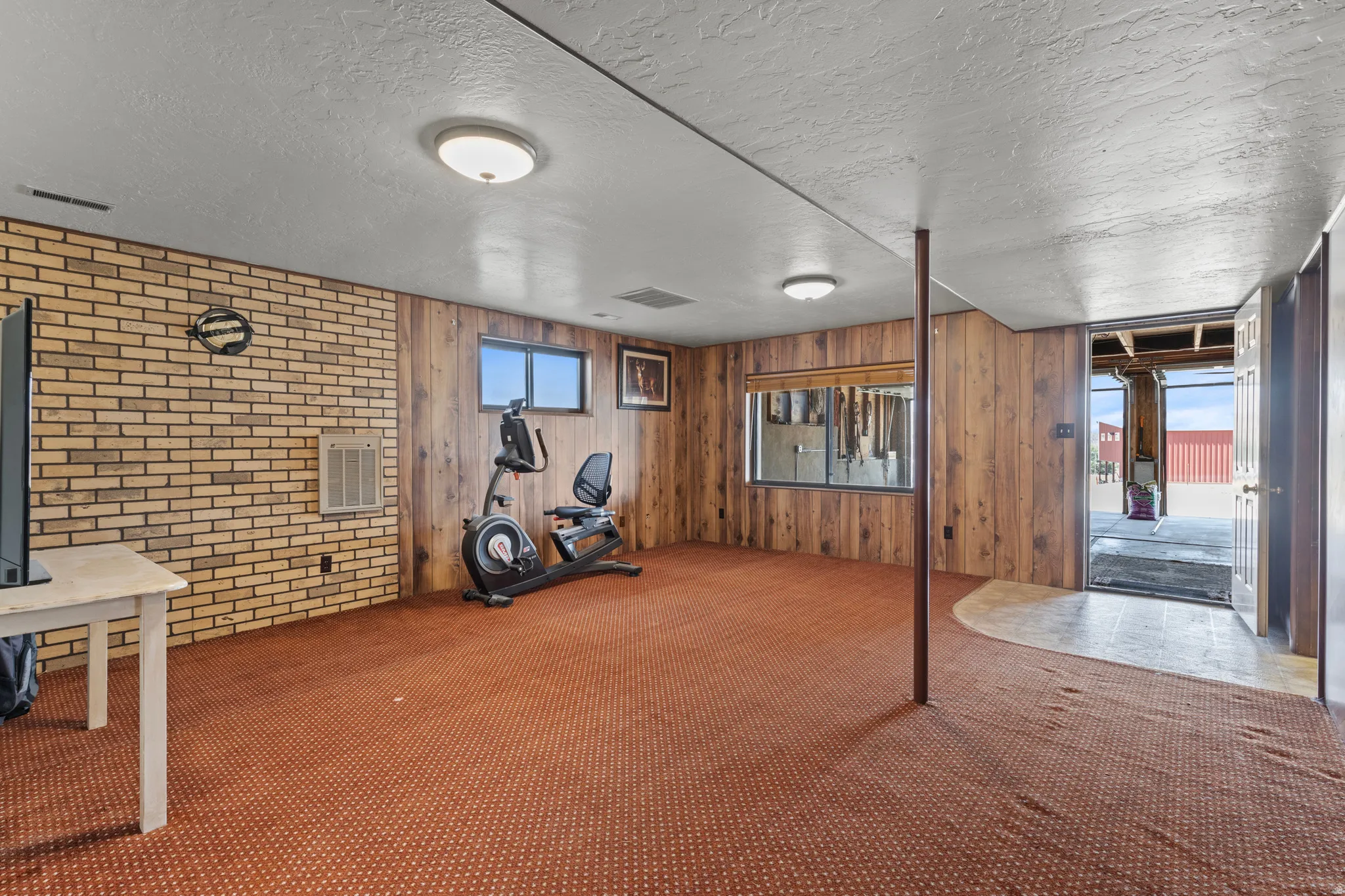 Carpeted interior space featuring wood-panel walls, exposed brick accent, and  windows