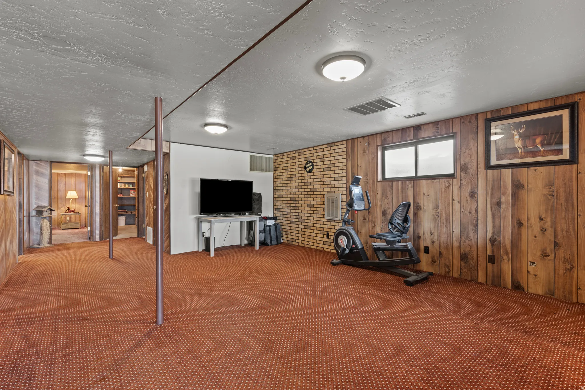 Expansive carpeted room featuring a mix of wood paneling and brick accent walls