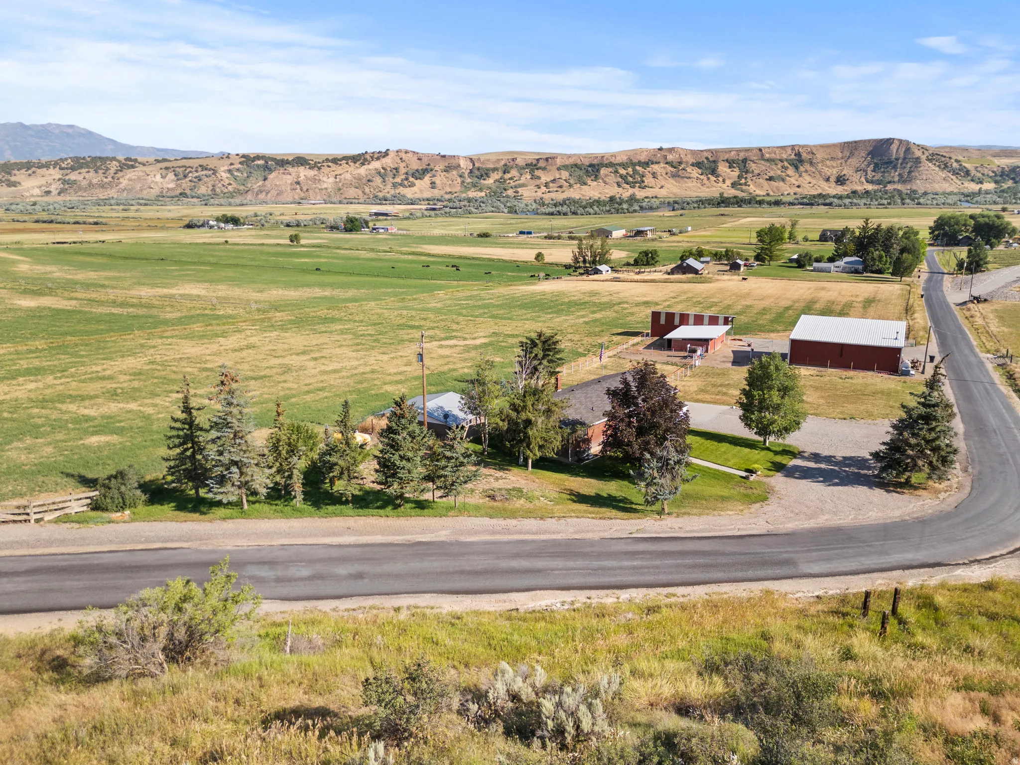 Expansive rural property featuring a main residence, outbuilding, mature trees, and a paved road frontage