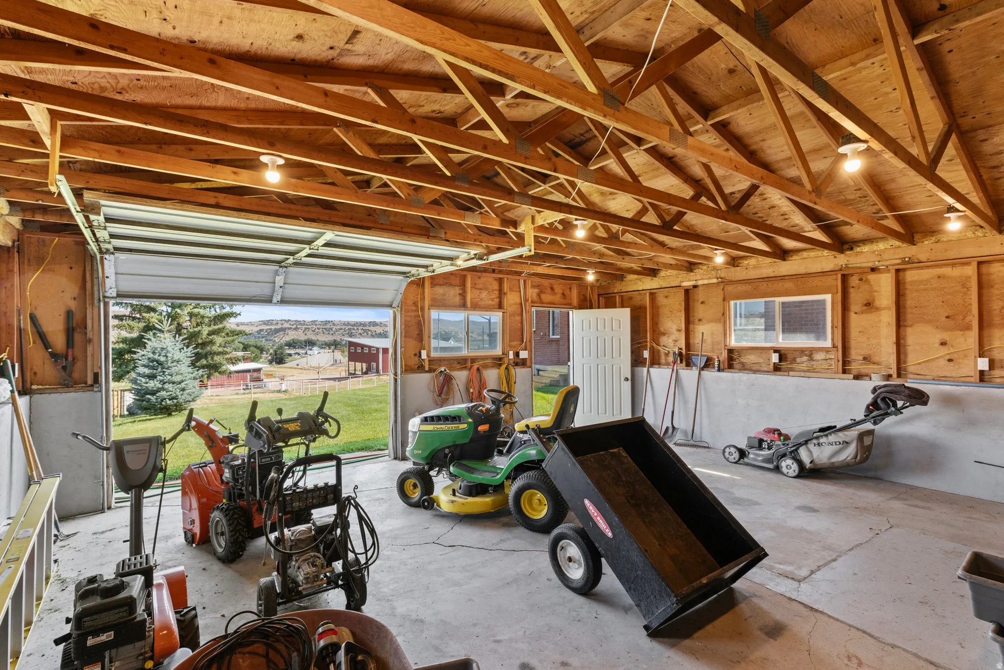 Spacious garage featuring a concrete floor, exposed wood beam ceiling, and panel walls