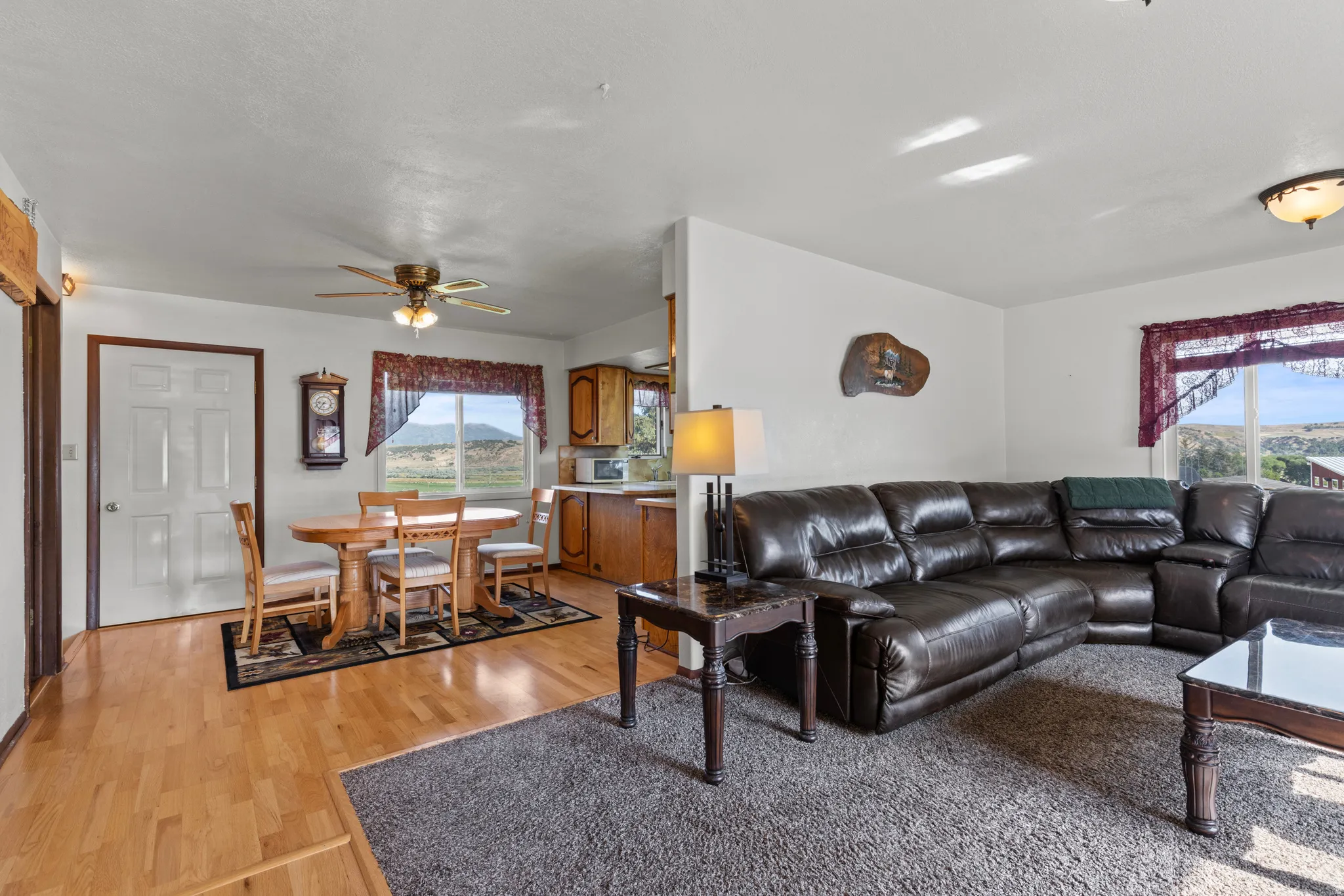 Open-concept living area featuring light wood-finish flooring, a neutral color palette, a ceiling fan, and abundant natural light from multiple windows