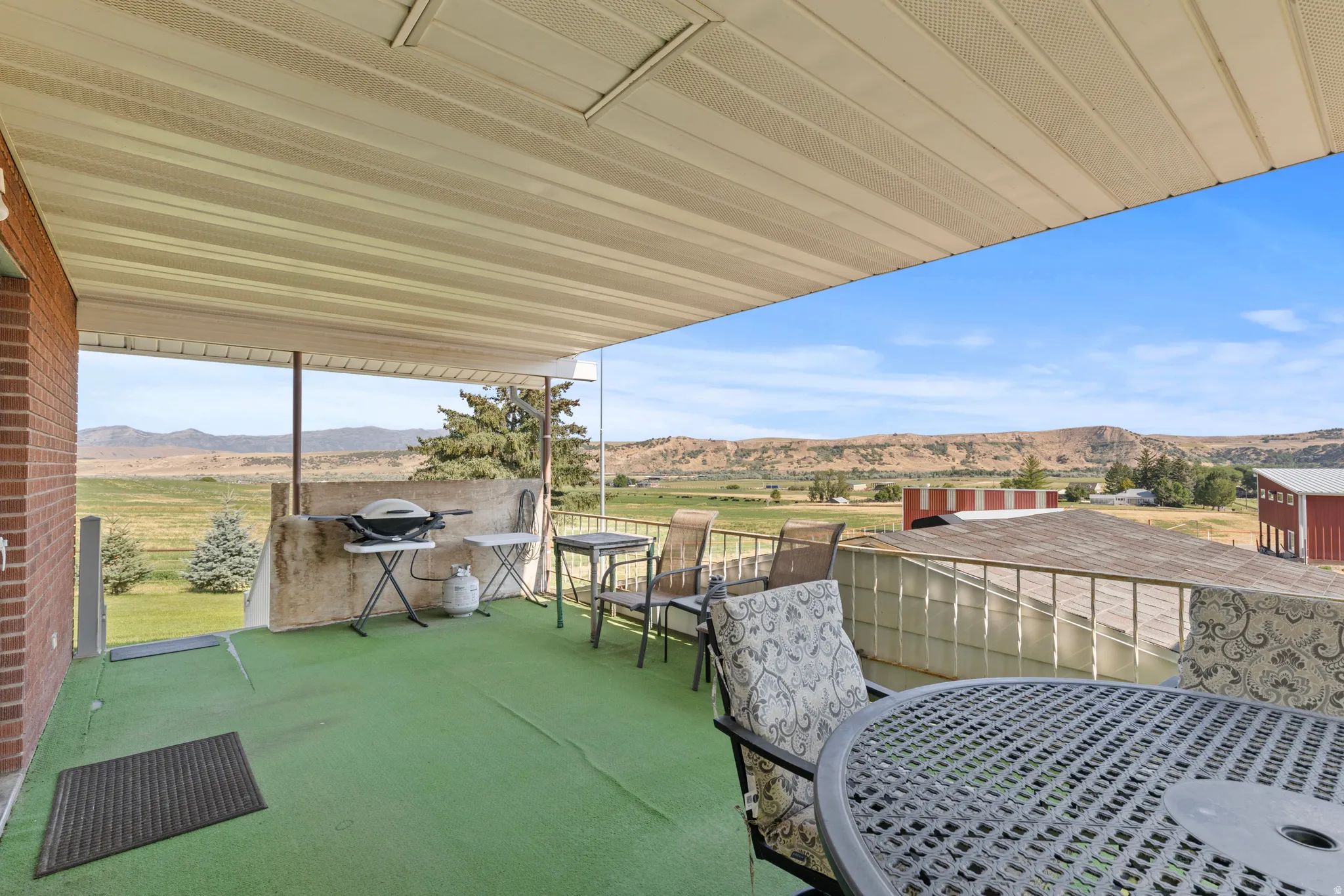 Covered outdoor deck area featuring a green outdoor carpet and a brick exterior wall