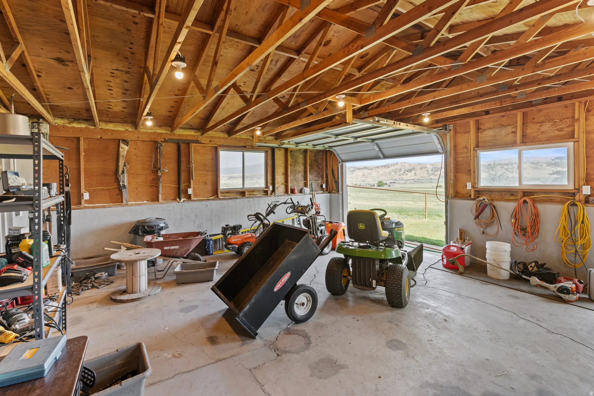 Spacious interior garage featuring exposed wood framing, concrete flooring, two windows, and an open garage door