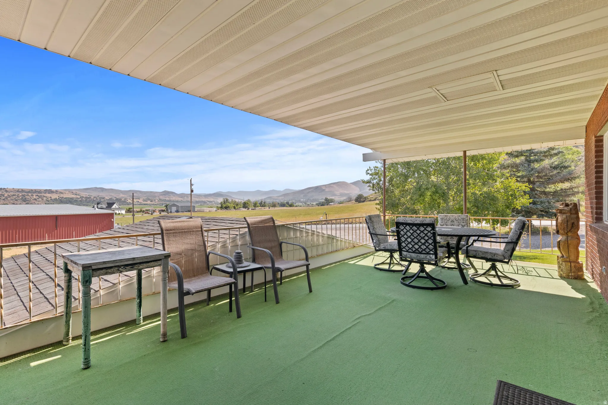 Expansive covered deck featuring a green outdoor carpet and a brick exterior wall