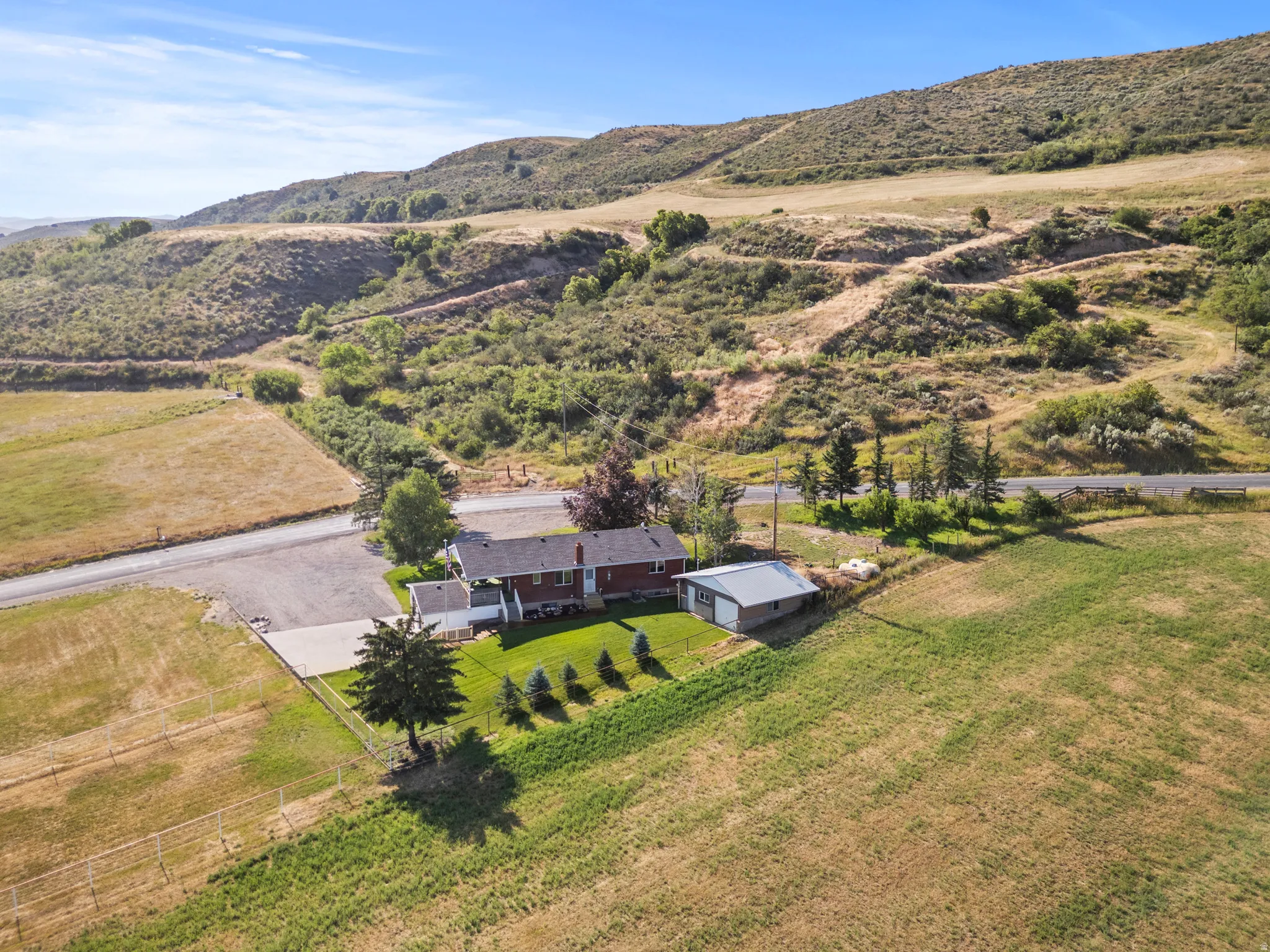 Expansive rural property featuring a red brick residence with a white front porch and a detached metal-roofed garage