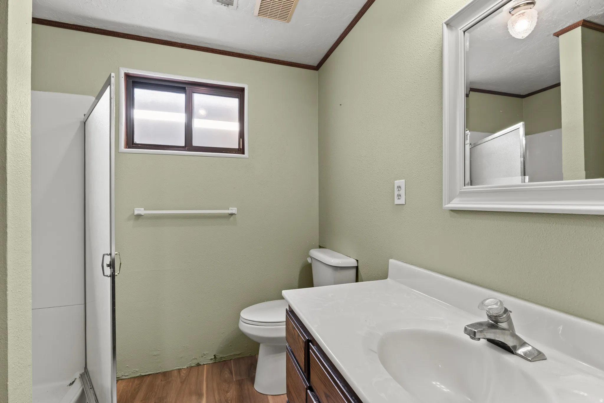 Bathroom featuring a wood-finish vanity with a white countertop and integrated sink, a framed wall mirror, and a shower enclosure