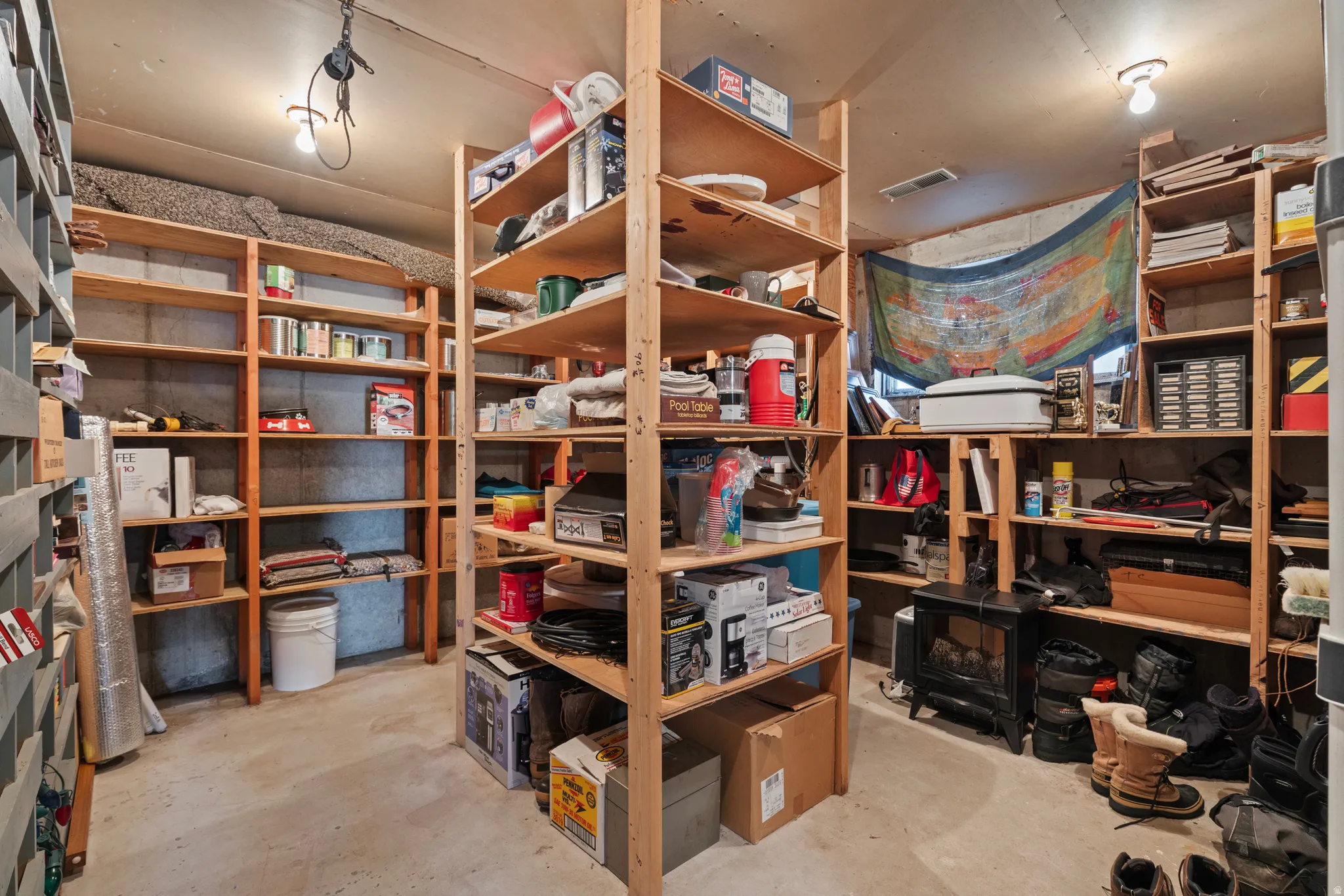 Spacious storage area featuring concrete flooring, exposed concrete walls, and multiple built-in wooden shelving units