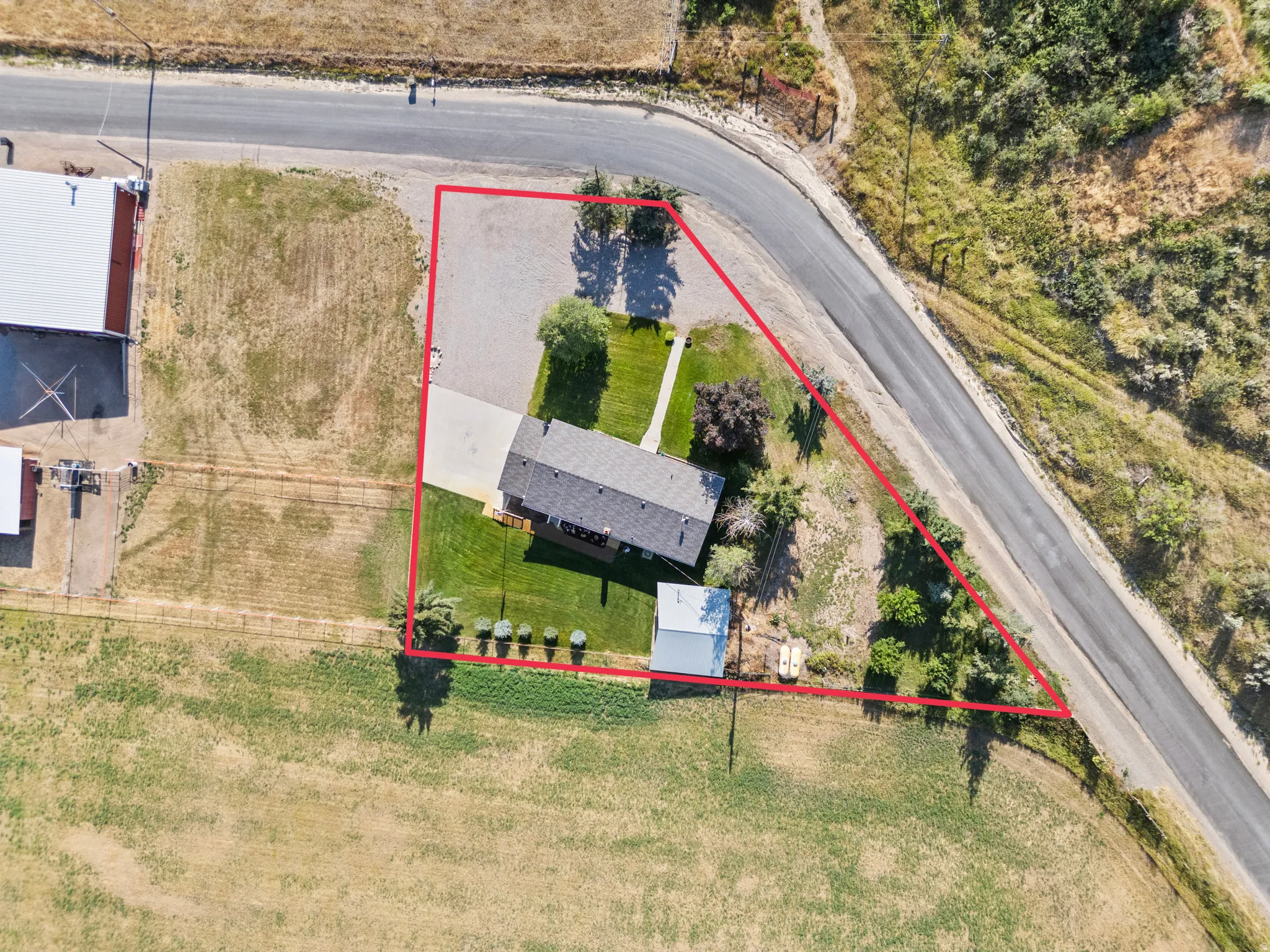 Overhead perspective showcasing a single-story residence with a shingle roof, a gravel driveway, and a detached outbuilding