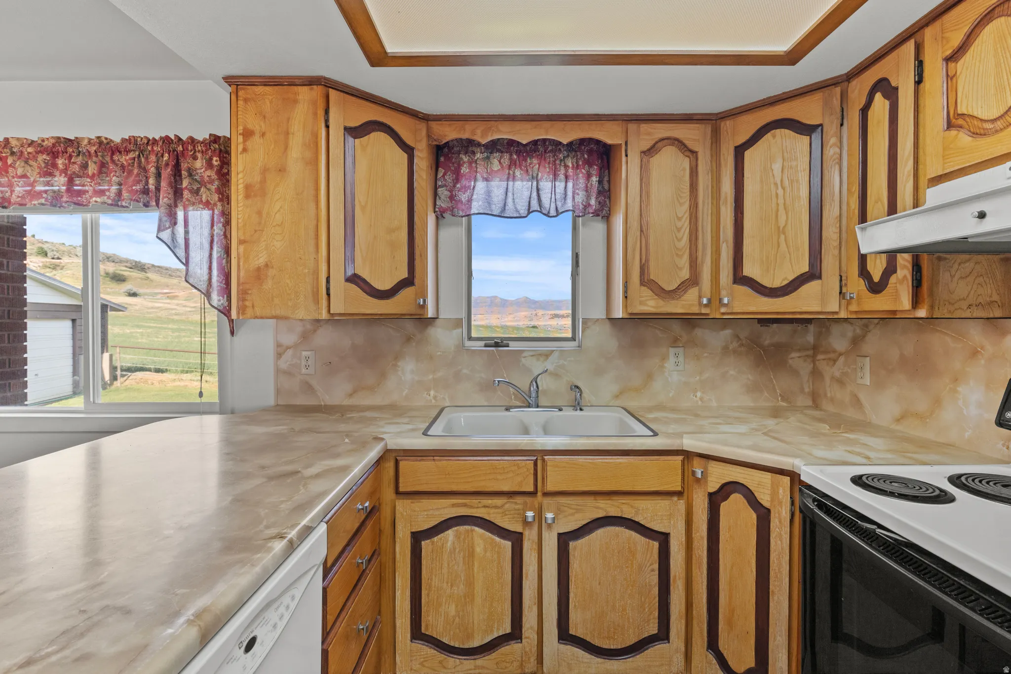 Kitchen featuring wood cabinetry, light-toned countertops, and a double basin sink with a window overhead