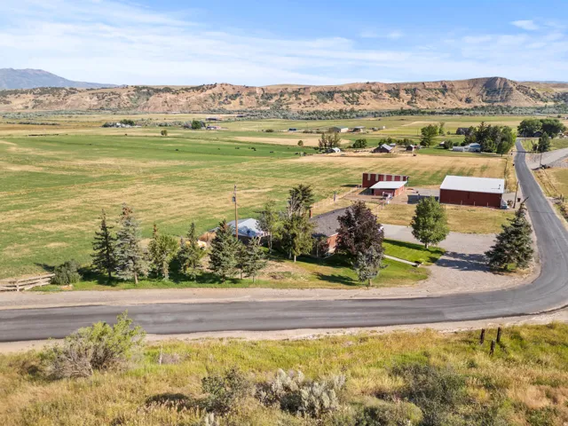 Expansive rural property featuring a main residence, outbuilding, mature trees, and a paved road frontage