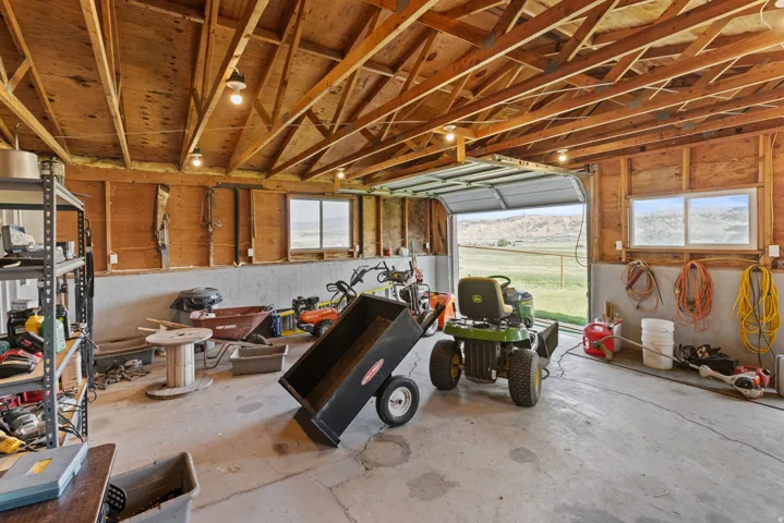 Spacious interior garage featuring exposed wood framing, concrete flooring, two windows, and an open garage door