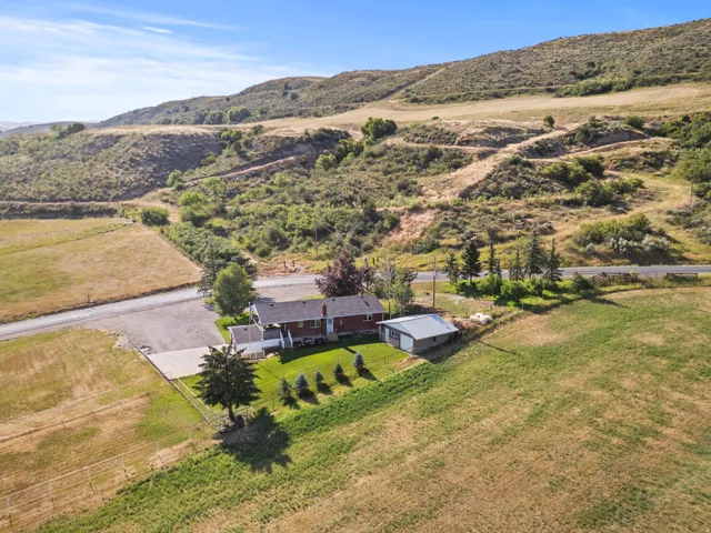 Expansive rural property featuring a red brick residence with a white front porch and a detached metal-roofed garage