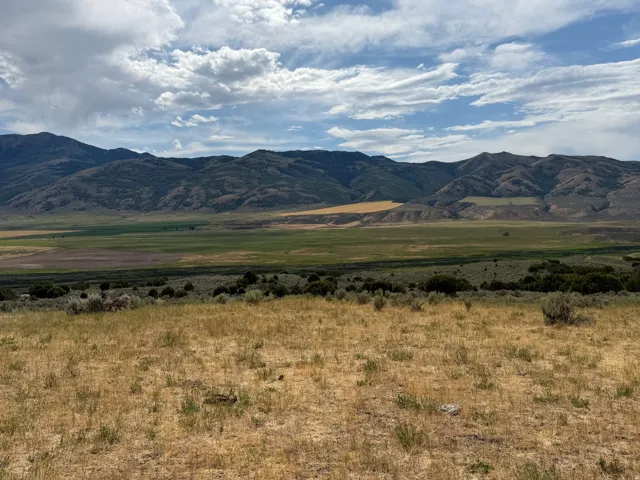 Expansive natural landscape featuring rolling hills and distant mountains under a dynamic sky