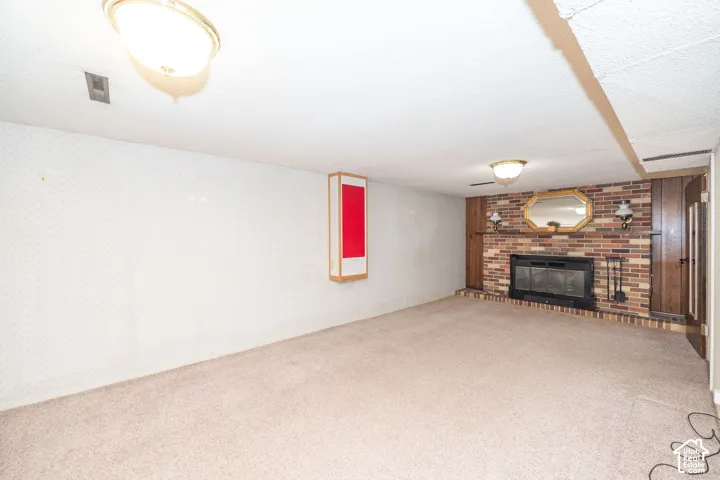 Carpeted interior space featuring a brick fireplace with a raised hearth, wood paneling, and an overhead light fixture