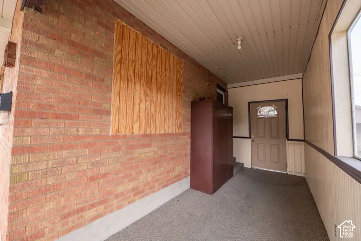 Covered porch entry featuring brick exterior walls and a paneled ceiling