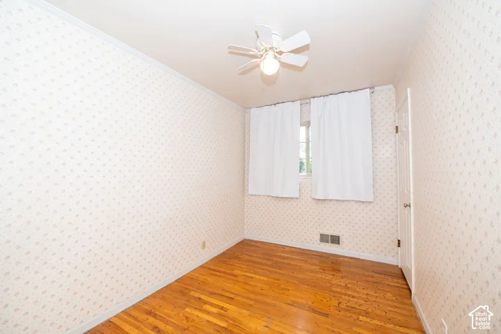 Room featuring wood-finish flooring, a ceiling fan with integrated lighting, and a single window with white curtains