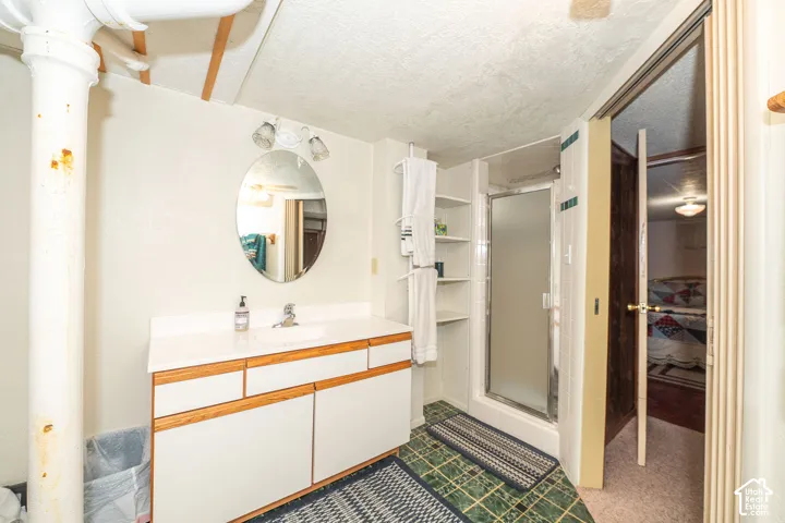 Bathroom featuring a white vanity with wood-finish trim, oval mirror, wall-mounted light fixture, and a glass-enclosed shower with integrated shelving