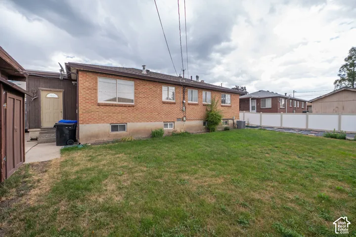 Expansive backyard with a manicured lawn, brick exterior, multiple windows, and a privacy fence