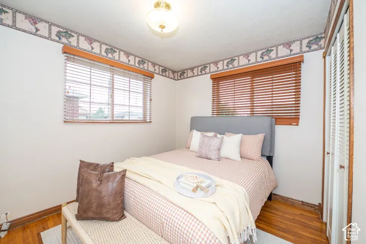 Interior room featuring wood-finish flooring, two windows with wood blinds, a ceiling-mounted light fixture, and a bi-fold closet door