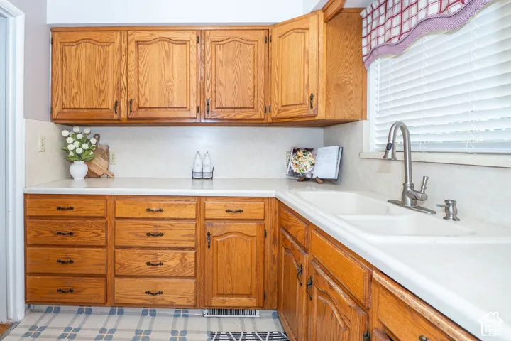 Kitchen featuring wood-finish cabinetry, white countertops, a double basin sink, and a brushed nickel faucet