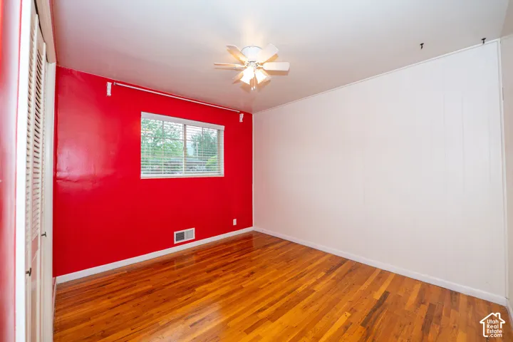 Room featuring wood-finish flooring, a ceiling fan, a window with blinds, and contrasting red and white wall finishes