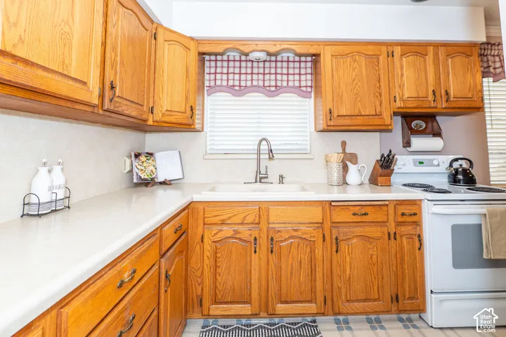Kitchen featuring wood cabinetry, light-toned countertops, a white sink with a gooseneck faucet, and a white freestanding range