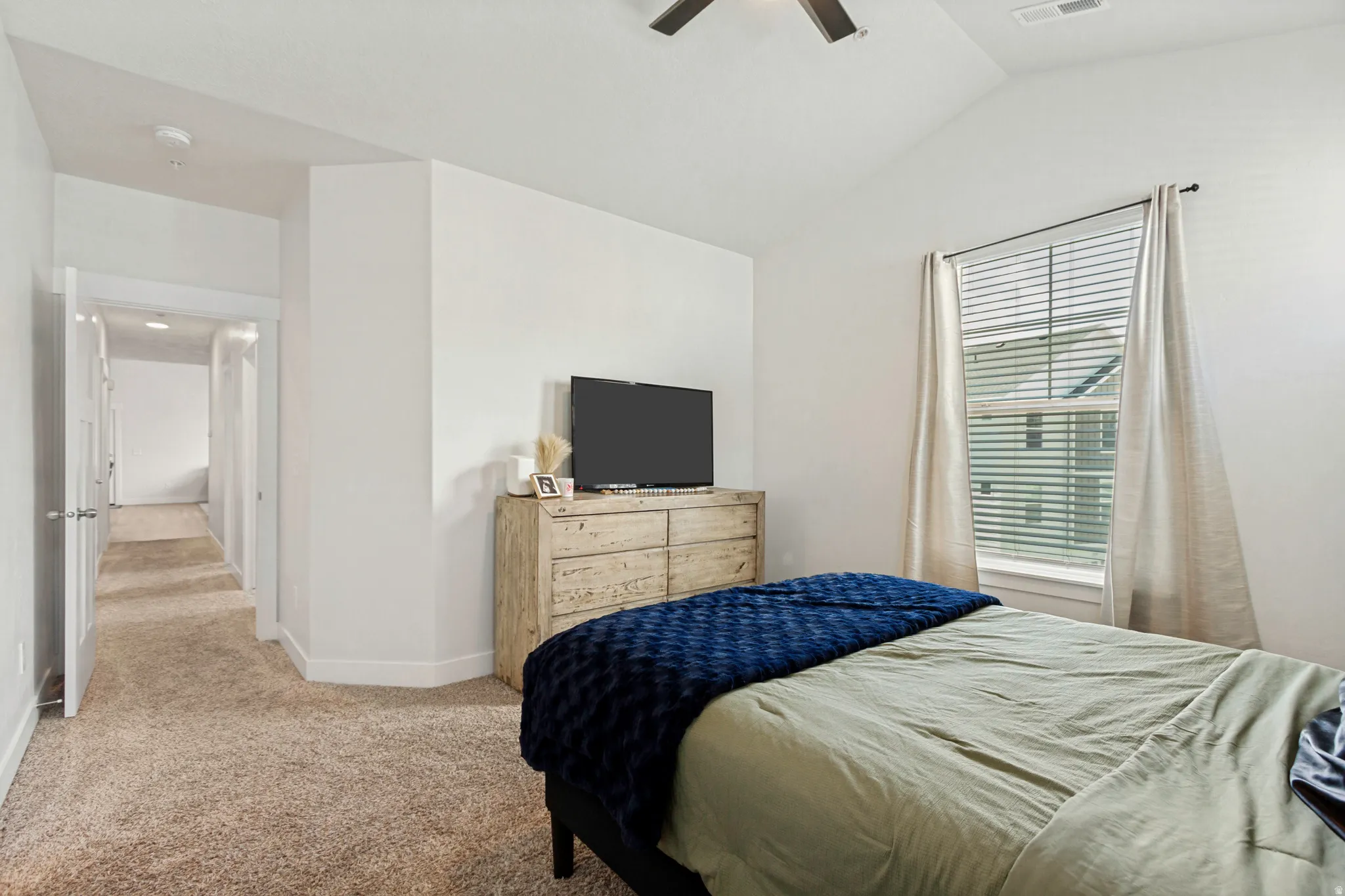 Bedroom featuring vaulted ceilings, plush carpeting, a ceiling fan, and a window with blinds and drapes
