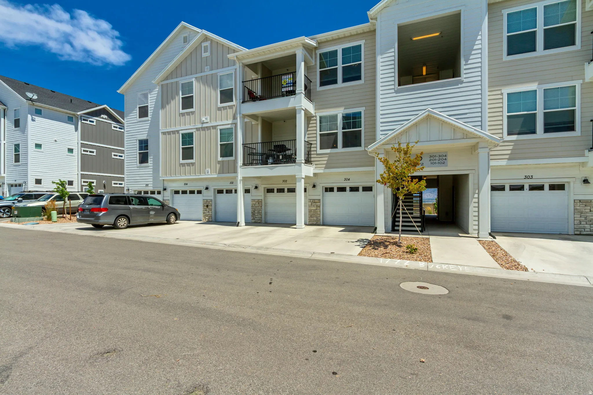 Multi-story residential building featuring light-colored siding, multiple balconies with black railings, and several attached garages with white doors