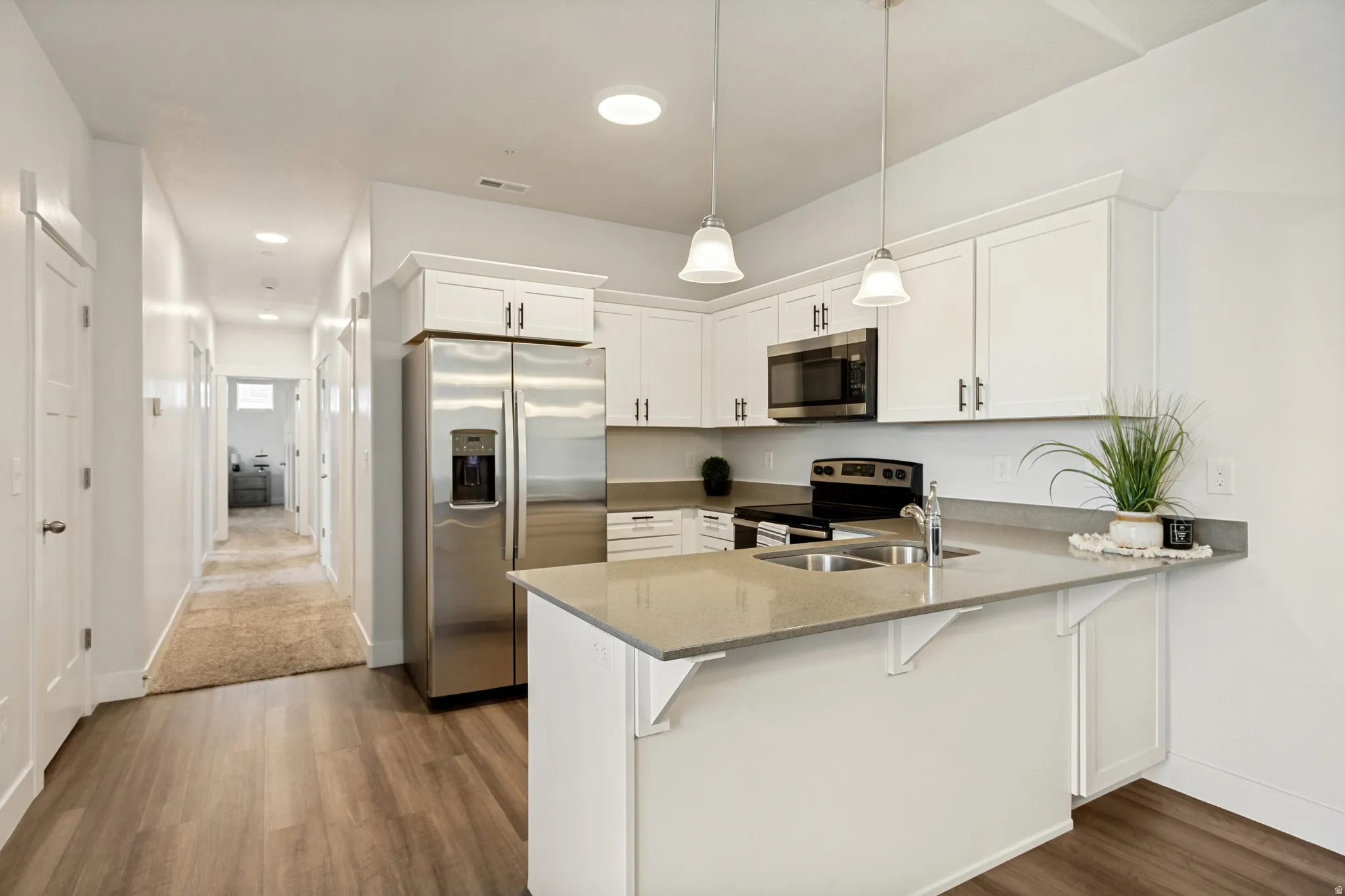 Contemporary kitchen featuring white cabinetry, stainless steel appliances, pendant lighting, and a peninsula with countertop seating