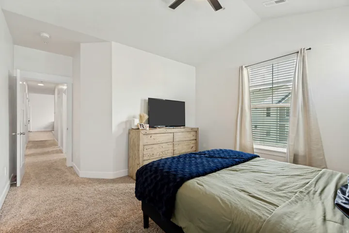 Bedroom featuring vaulted ceilings, plush carpeting, a ceiling fan, and a window with blinds and drapes