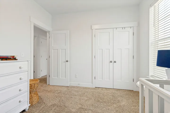 Neutral-toned carpeting extends throughout this room, featuring a pair of white paneled closet doors with polished hardware