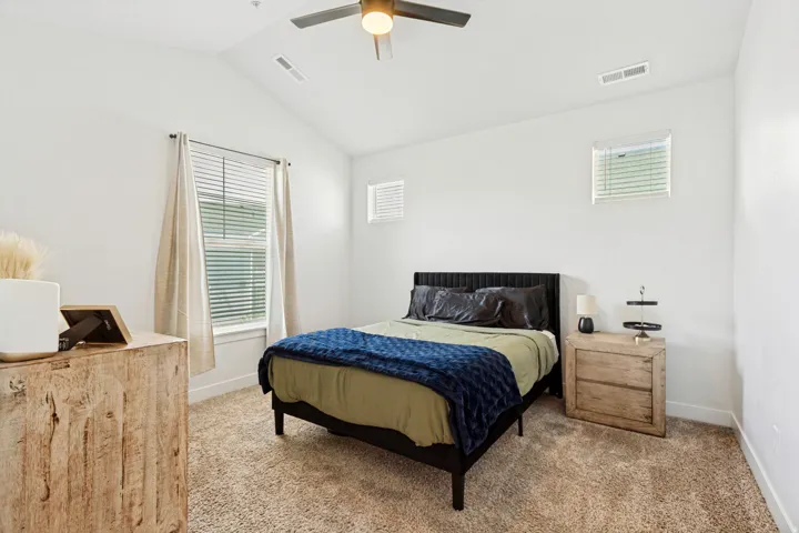 Carpeted room featuring a vaulted ceiling with a flush-mount ceiling fan