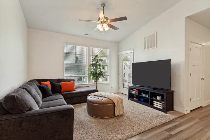 Vaulted ceiling with a ceiling fan light fixture, multiple windows with blinds, and light-tone wood-finish flooring