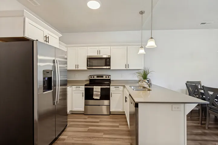 Modern kitchen featuring white shaker cabinetry, stainless steel appliances, light-toned countertops, and wood-finish flooring