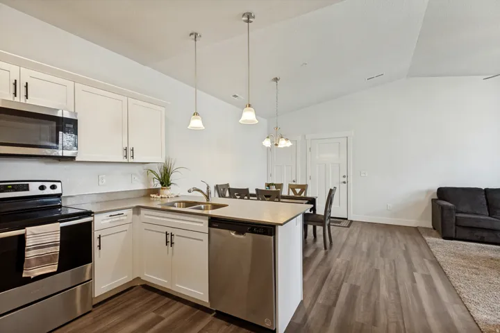 Open-concept living area featuring a kitchen with white cabinetry, stainless steel appliances, and a peninsula with pendant lighting