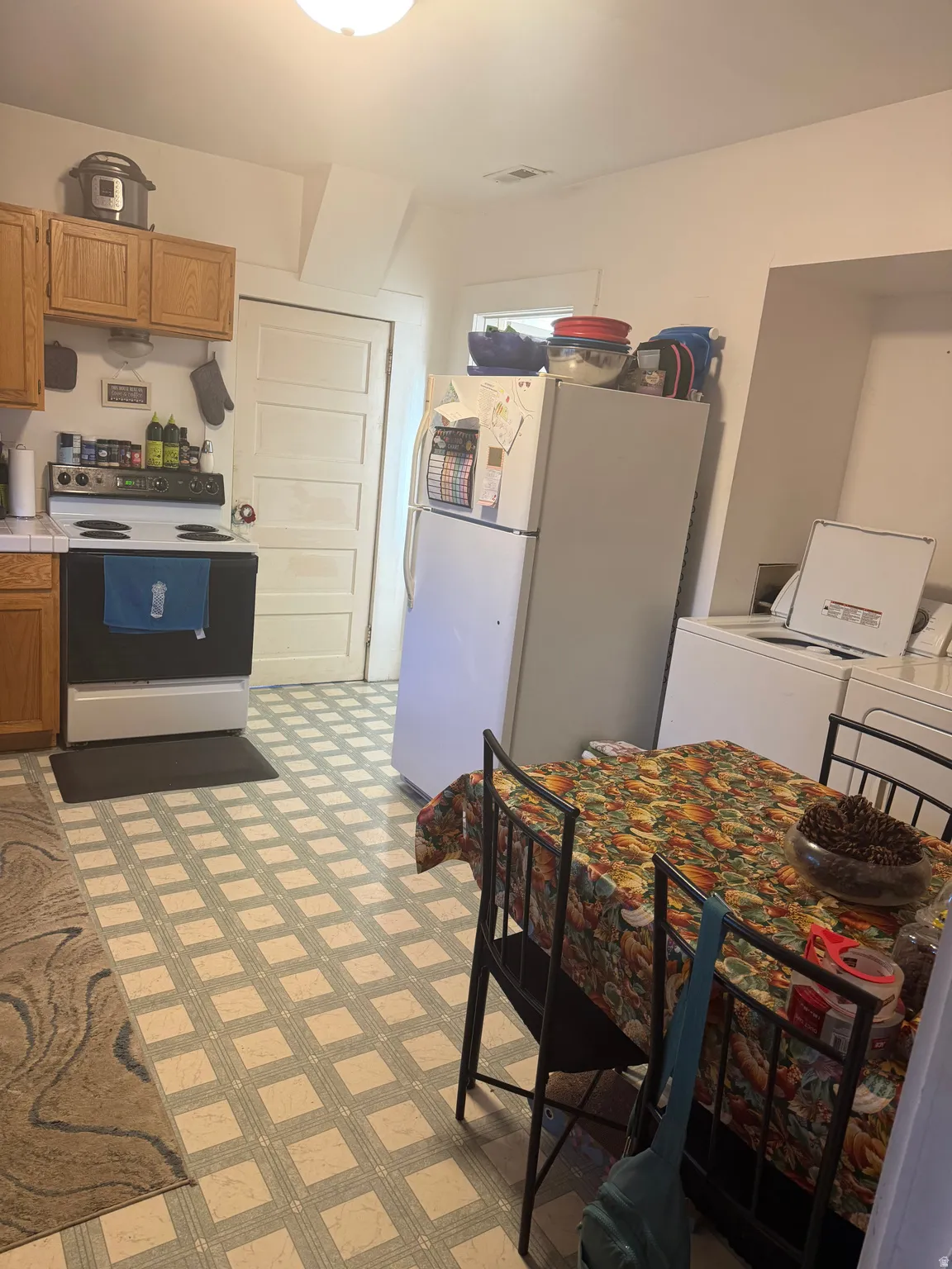 Kitchen space featuring light wood cabinetry, white appliances, and a patterned tile-finish floor