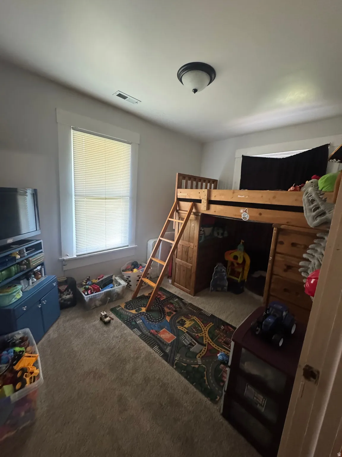 Carpeted room featuring a window with blinds, overhead flush mount lighting, and a visible ceiling vent