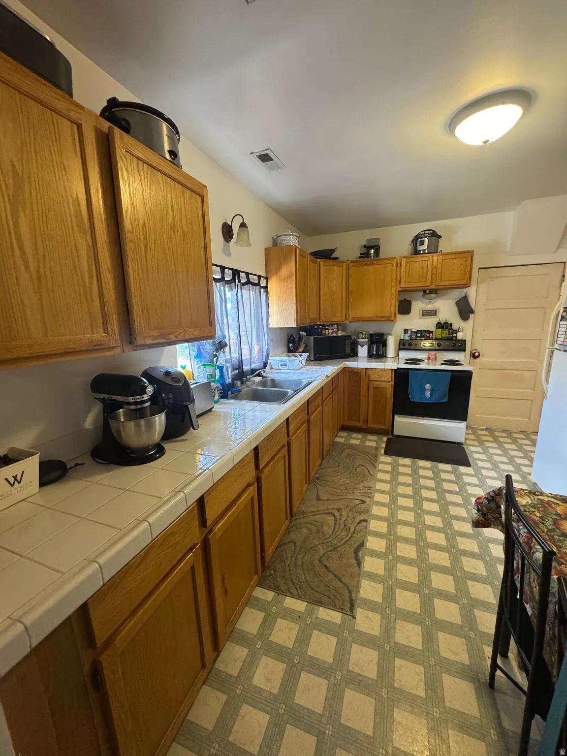 Kitchen featuring extensive wood-finish cabinetry, tile countertops, a double basin sink, and patterned flooring