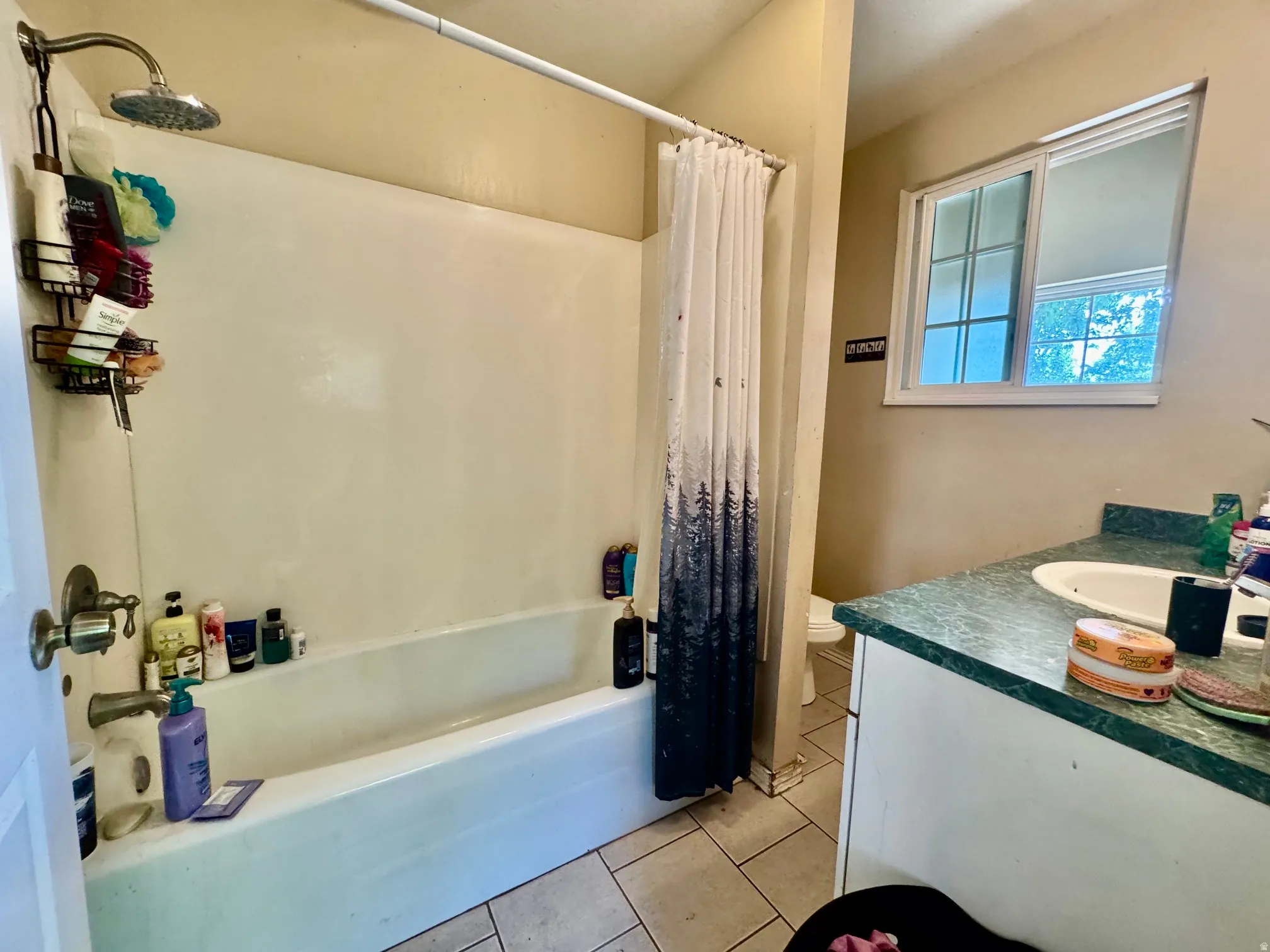 Bathroom featuring a white bathtub with an overhead shower, a single vanity with a green countertop and integrated sink, a window with frosted lower panes, and light-toned wall paint