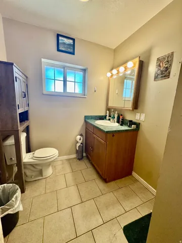 Bathroom with tiled flooring, a single vanity with wood-finish cabinetry, a built-in medicine cabinet with vanity lighting, and a frosted window