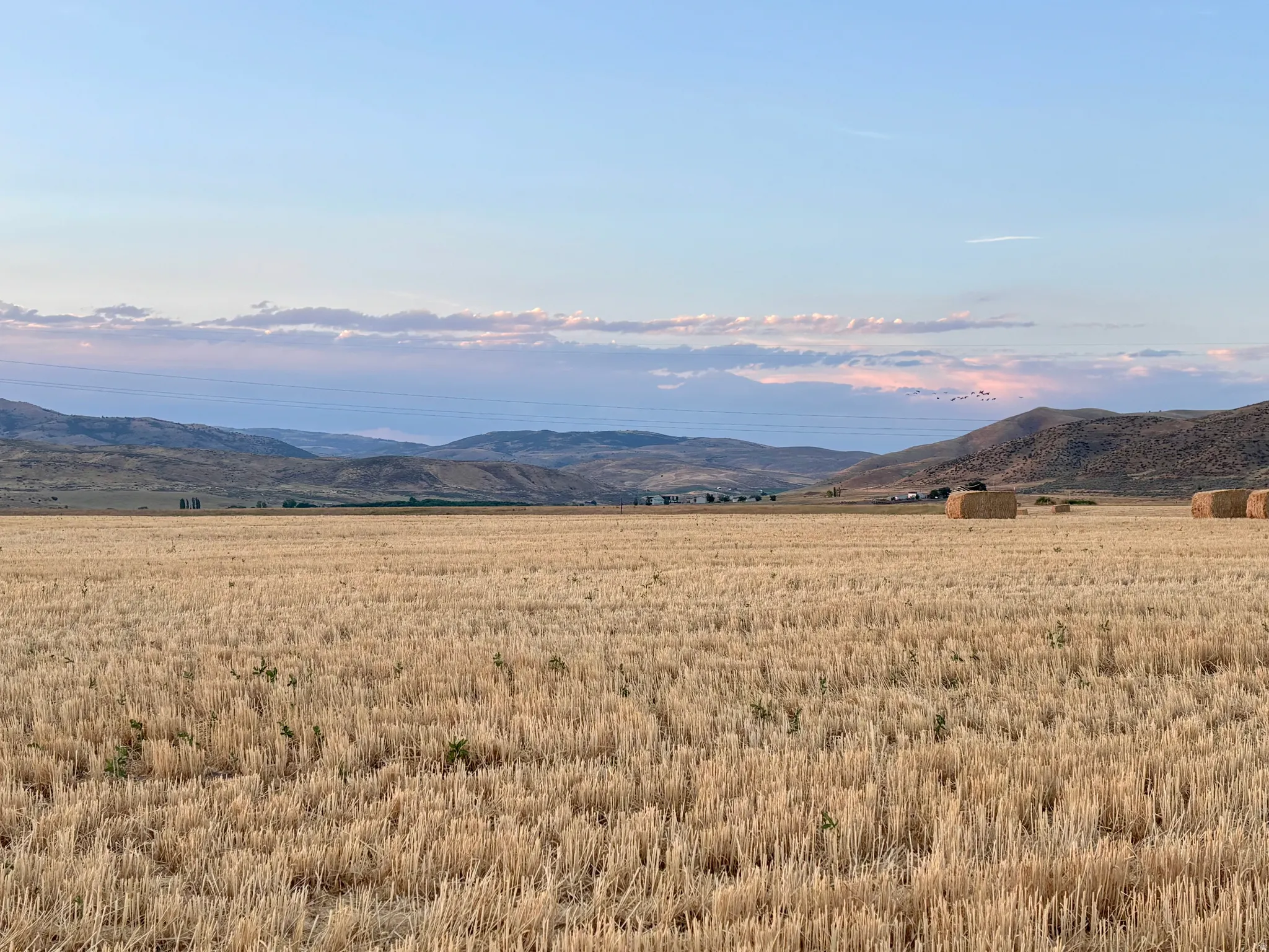 Expansive agricultural land featuring a harvested field with hay bales and distant hills