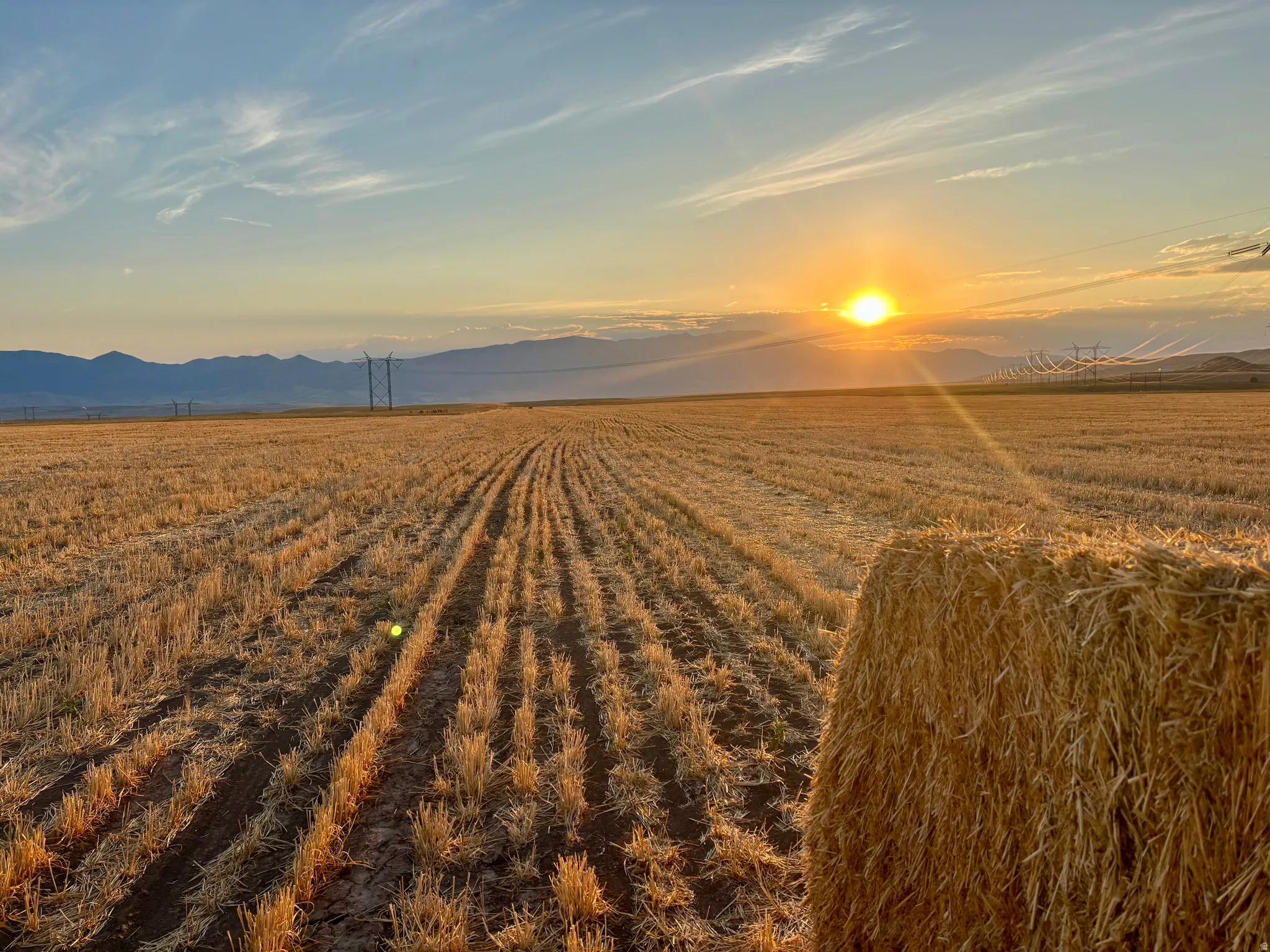 Expansive agricultural field with harvested crops, featuring a large hay bale in the foreground