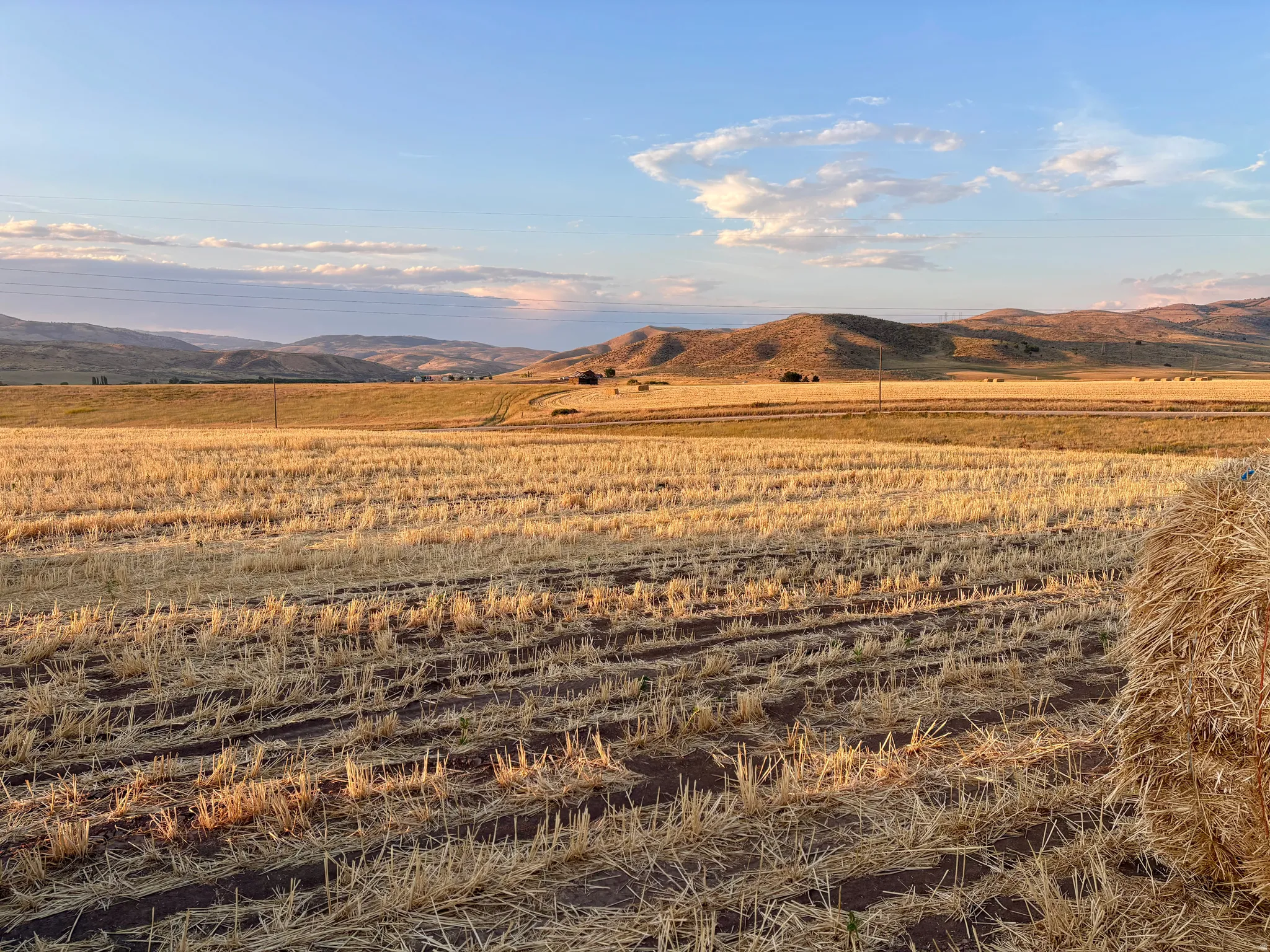 Expansive agricultural land featuring a golden harvested field and distant rolling hills