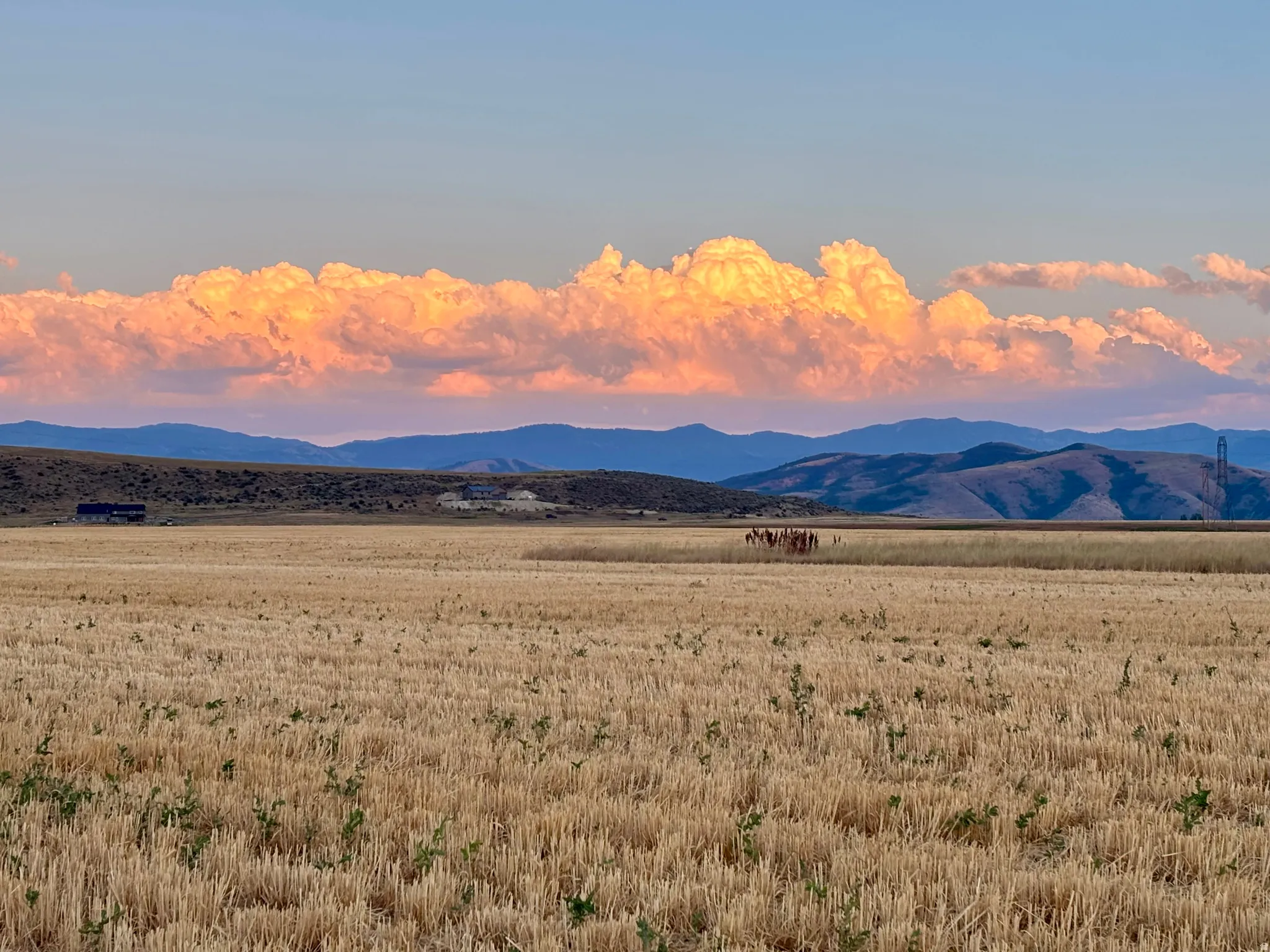 Expansive agricultural landscape featuring harvested fields, distant mountains, and a clear sky with prominent cloud formations