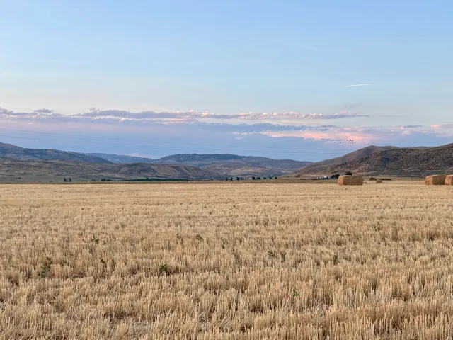 Expansive agricultural land featuring a harvested field with hay bales and distant hills