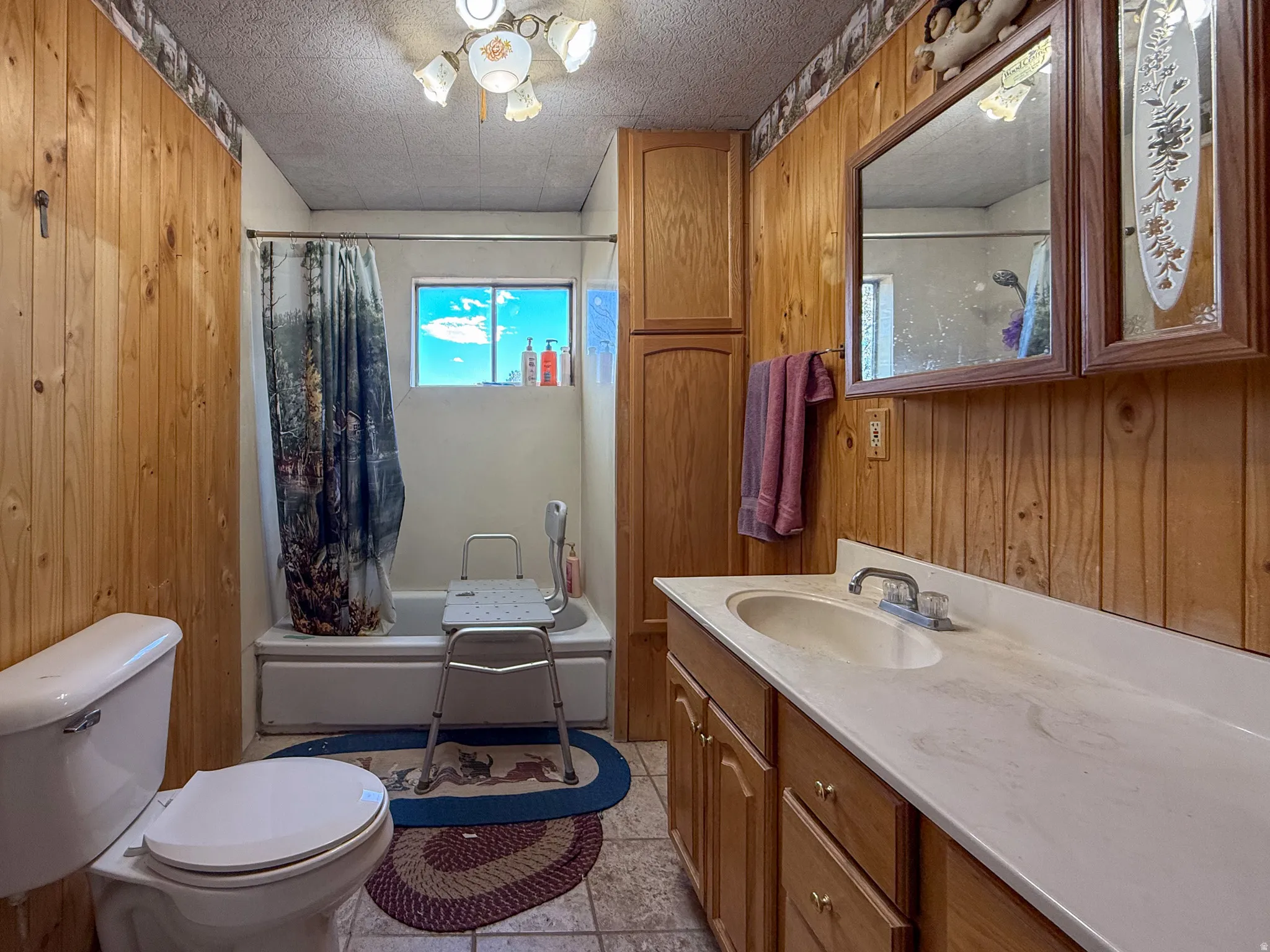 Bathroom featuring wood-paneled walls, a single vanity with an integrated sink, a built-in medicine cabinet, and a bathtub with an overhead shower